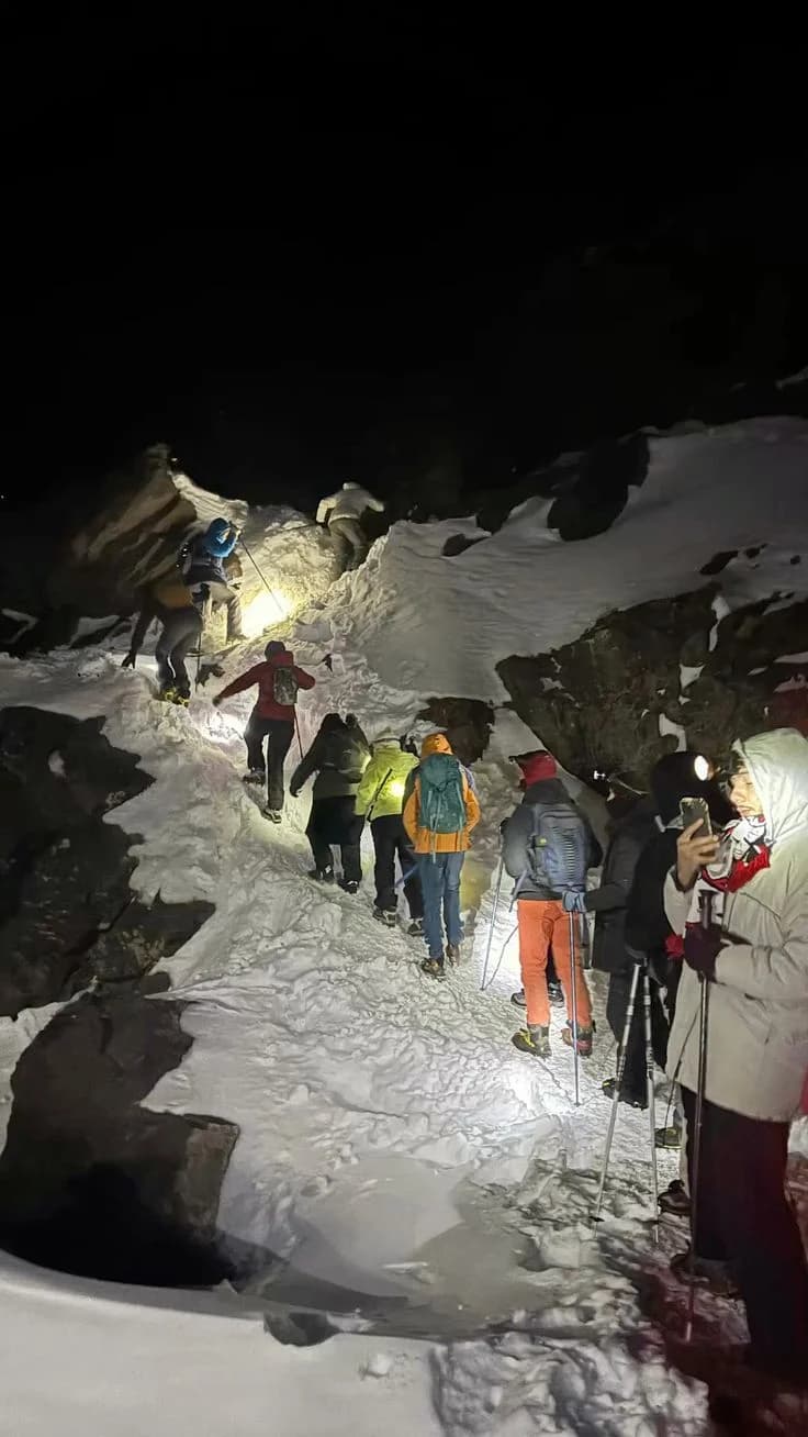 Hikers climbing a snowy trail by headlamp before dawn