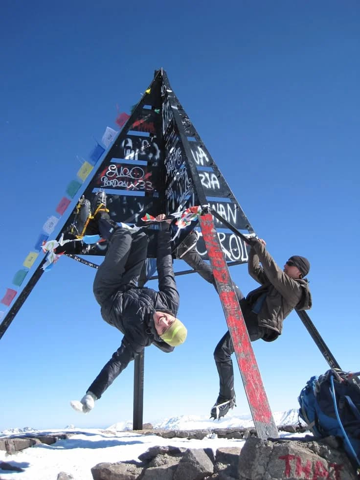 Two climbers celebrating on the metal Toubkal summit marker