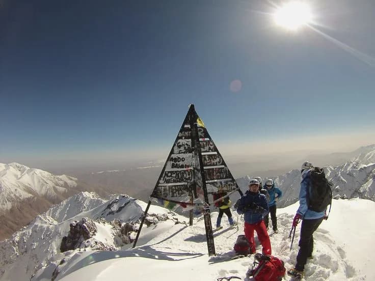 Climbers beside the Toubkal summit marker surrounded by snow